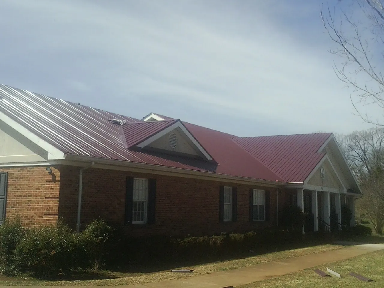 Red metal roof with gabled entries on a long brick building, from a Hail Damage Roof Repair job in New Hampton