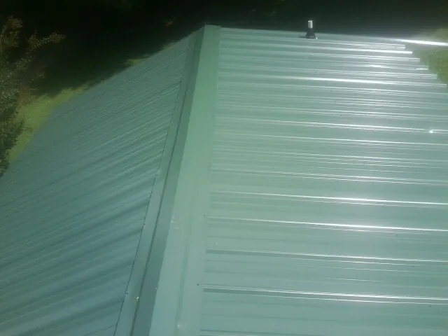 New green metal panels meeting at the ridge of a roof — Flat Roof Repair work by our crew in New Hampton
